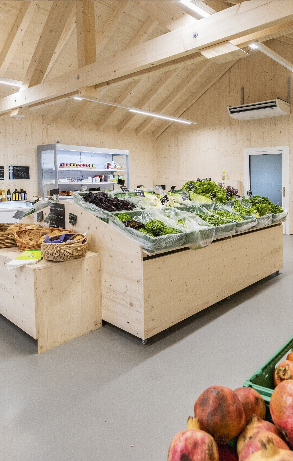 Gemüseauslage in einem hellen Laden mit Holzdecke und frischem Salat in Kisten