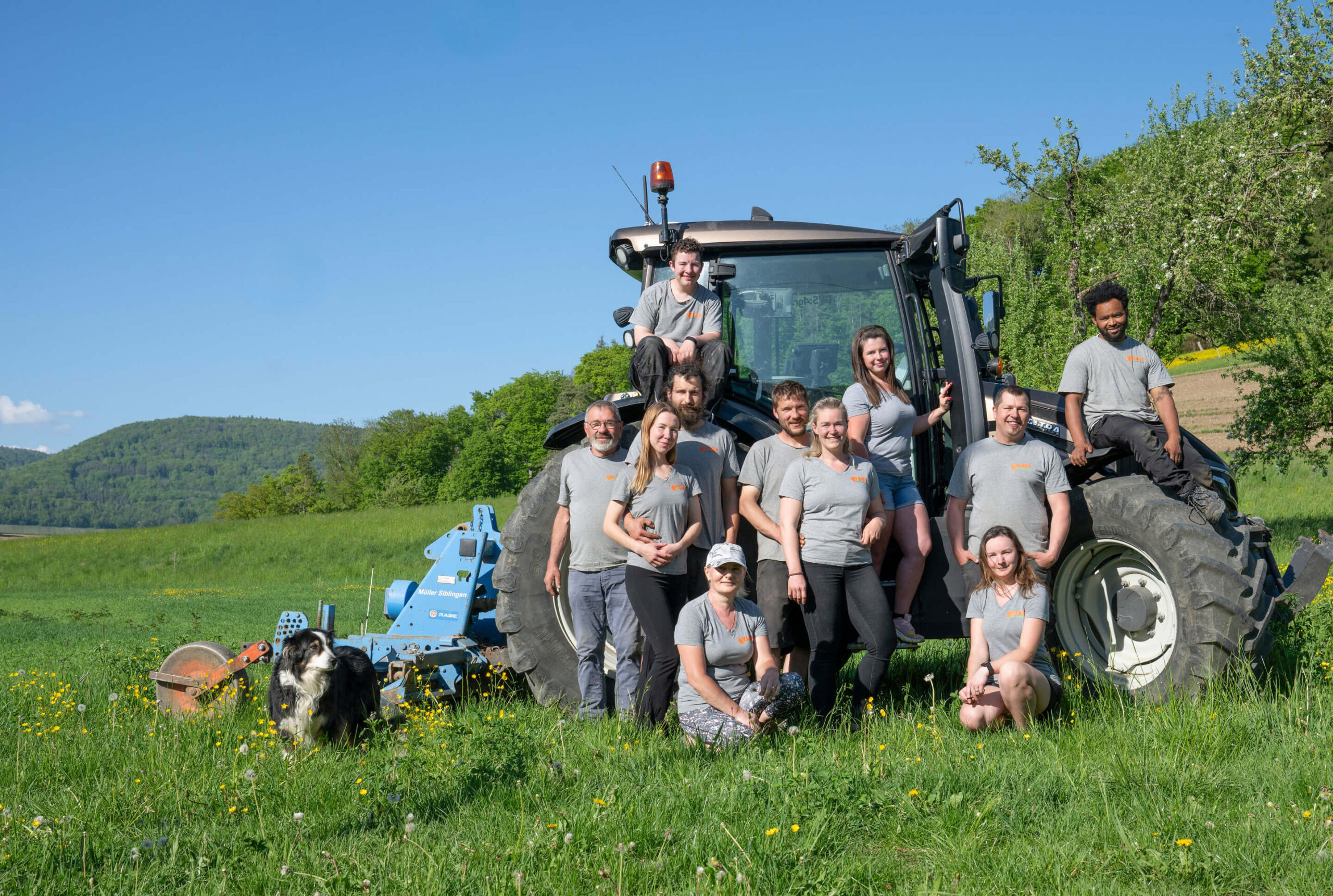 Weber Bioprodukte Team vor einem Traktor auf einer Wiese, mit Hund im Vordergrund