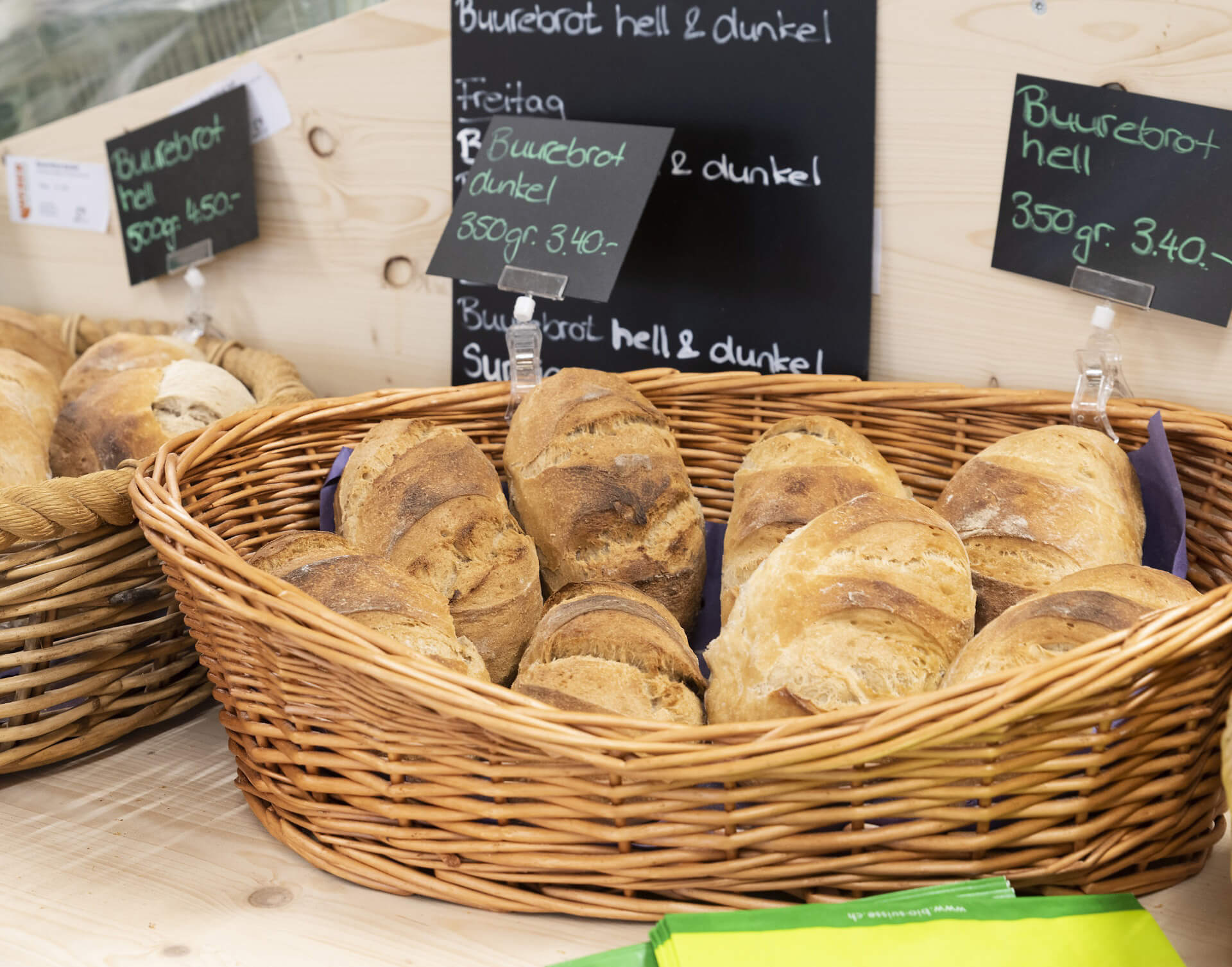 Körbe mit frischen Broten in einer Bäckerei, mit Tafeln für helles und dunkles Bauernbrot