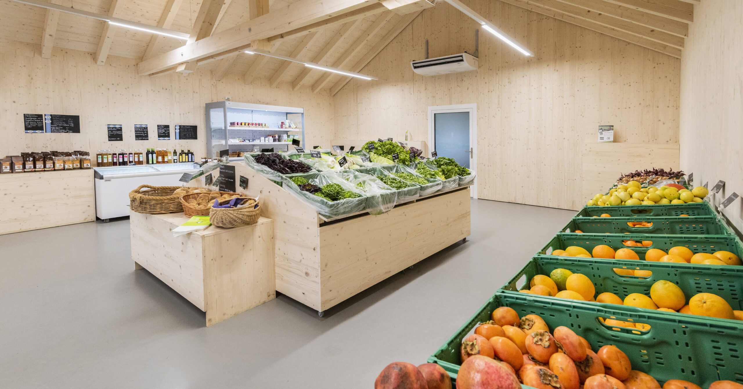 Innenraum eines kleinen Hofladens mit Holzregalen, frischem Gemüse und Obst in Kisten