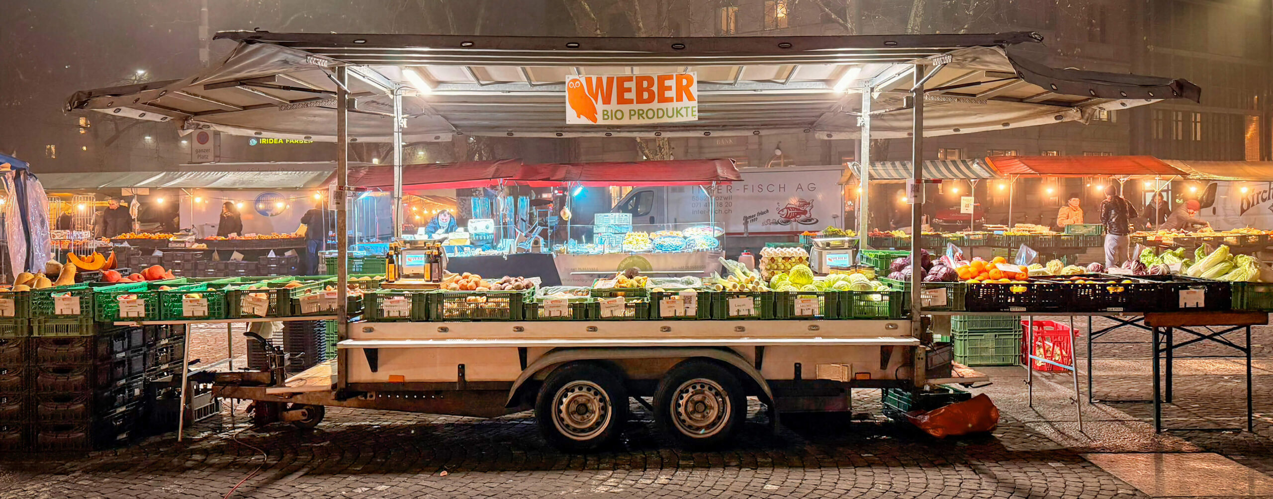 Gemüsestand auf einem Nachtmarkt mit Obst und Gemüse in Kisten unter einem Verkaufswagen
