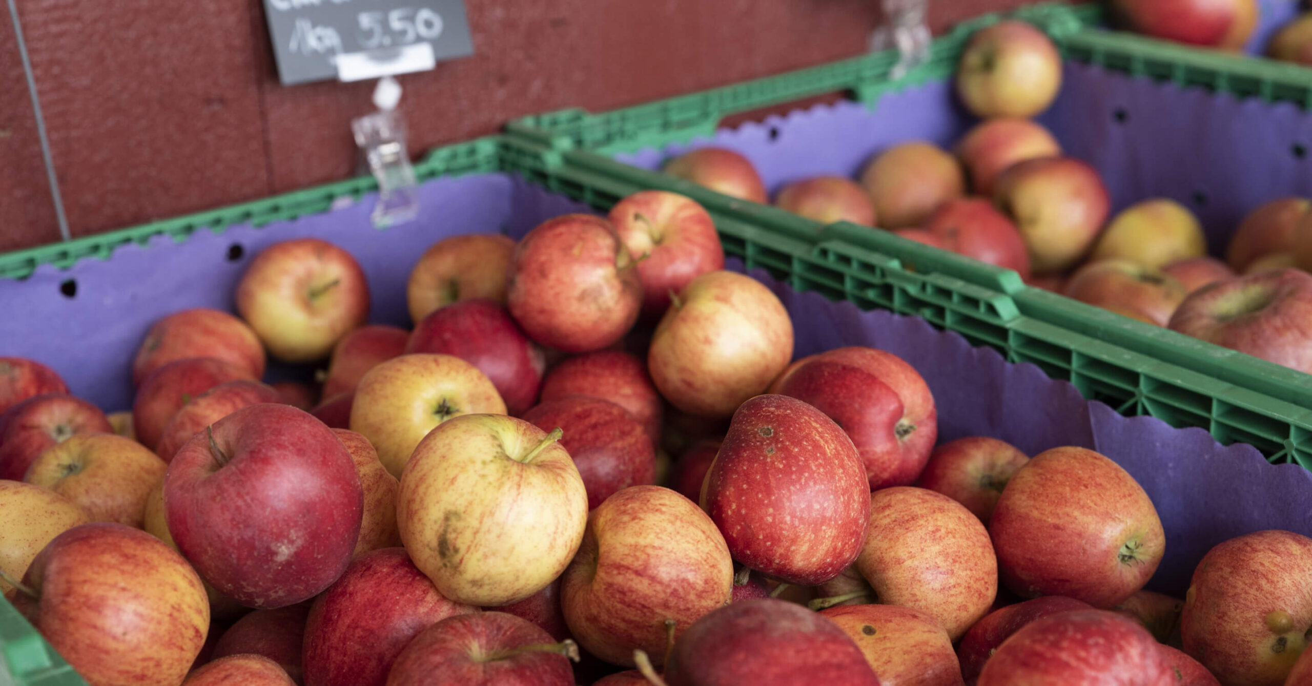 Kisten mit roten und gelben Äpfeln auf einem Markt, Preisschild im Hintergrund