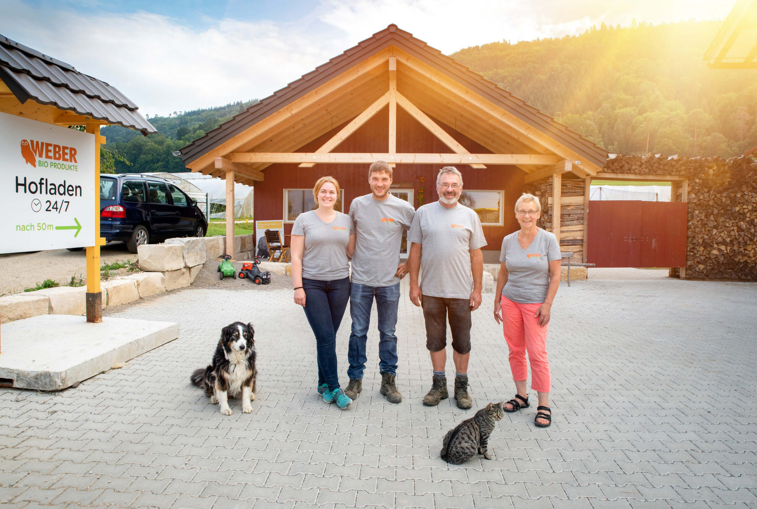 Weber Familie vor einem Hofladen von Weber Bio Produkte, mit Hund und Katze im Vordergrund