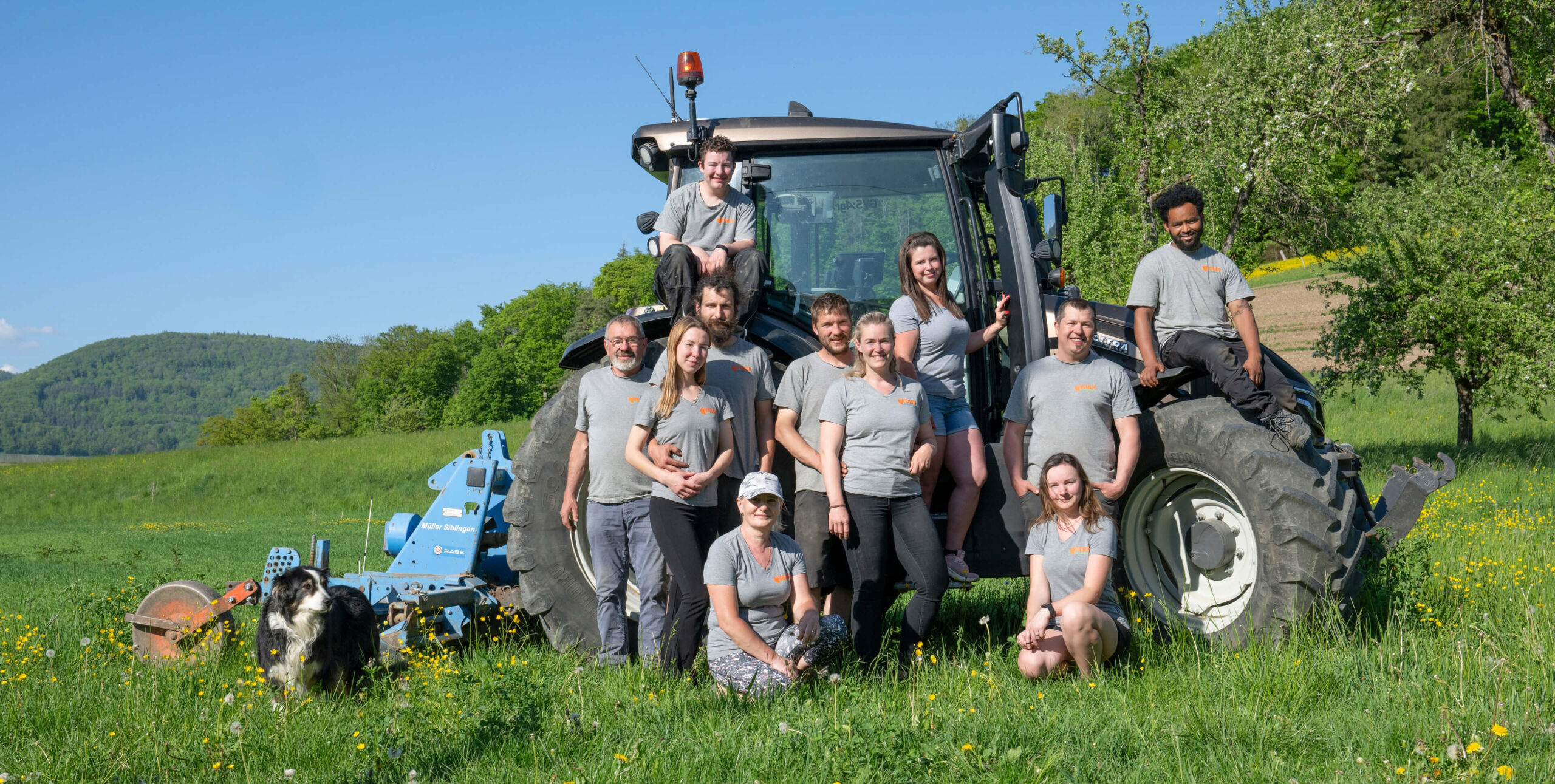 Weber Bioprodukte Team von Landwirten vor einem Traktor auf einer Wiese, mit Hund im Vordergrund